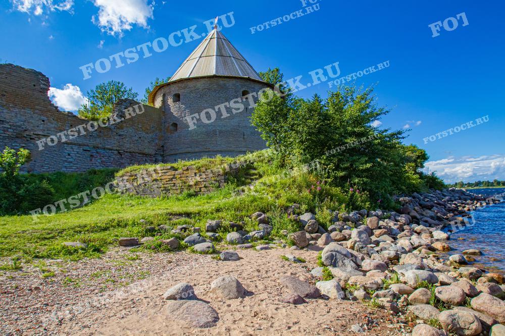 Это фотография показывает один из башенных элементов крепости Орешек в Ленинградской области, расположенной на берегу реки Невы. Каменные стены крепости и выступающая башня с конической крышей на фоне ясного неба создают ощущение могущества и исторической значимости. Фотография может быть использована в исторических исследованиях, туристических материалах и как элемент декора, вдохновляющий на размышления о прошлом.